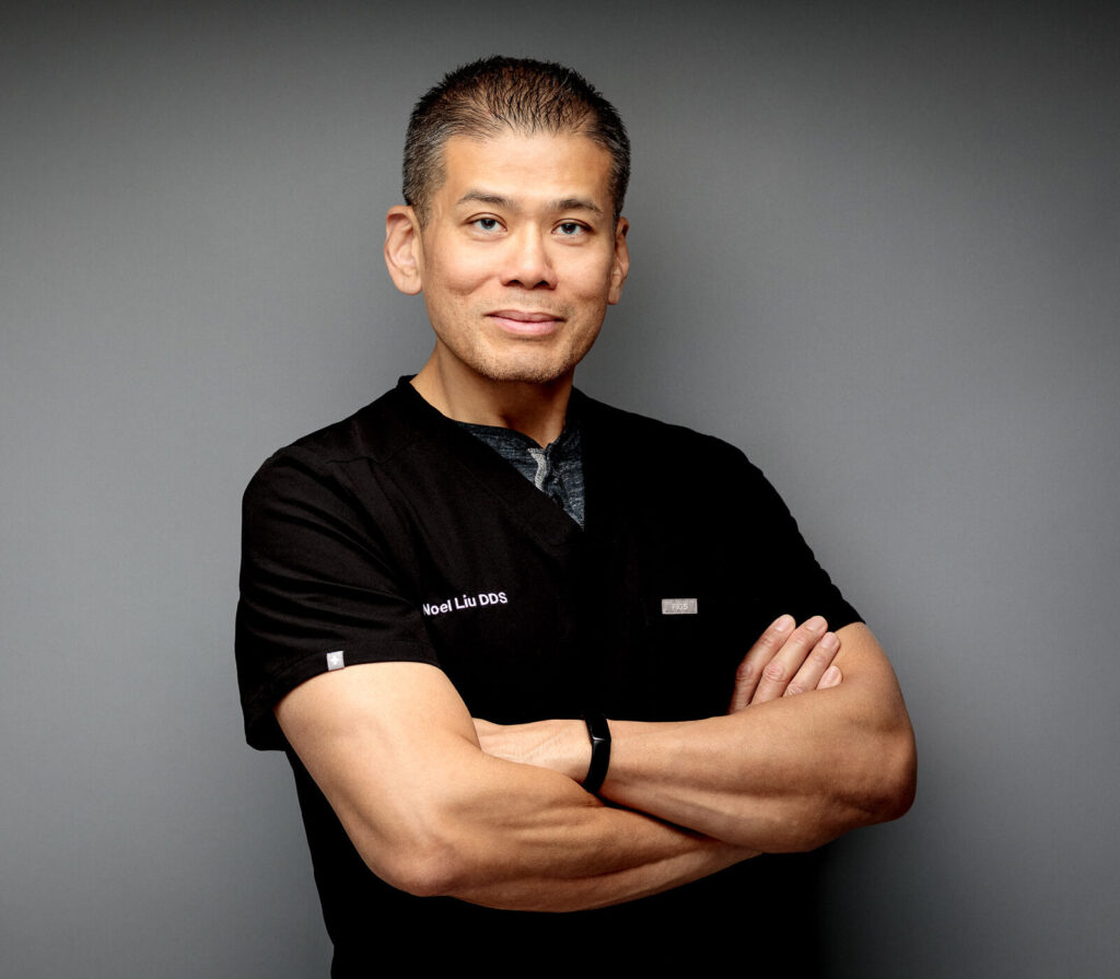Headshot of Dr. Noel Liu wearing black scrubs with arms folded