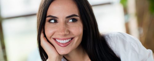 Photo of stunning adorable young lady hand touch cheek beaming smile imagine contemplate daydreaming apartment indoors.